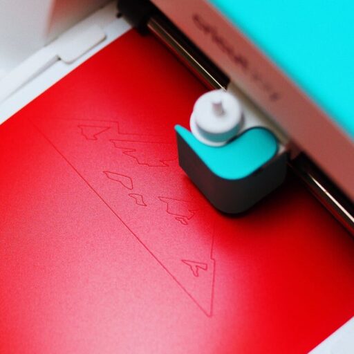 Close-up of a cutting machine engraving a pattern on red paper indoors.